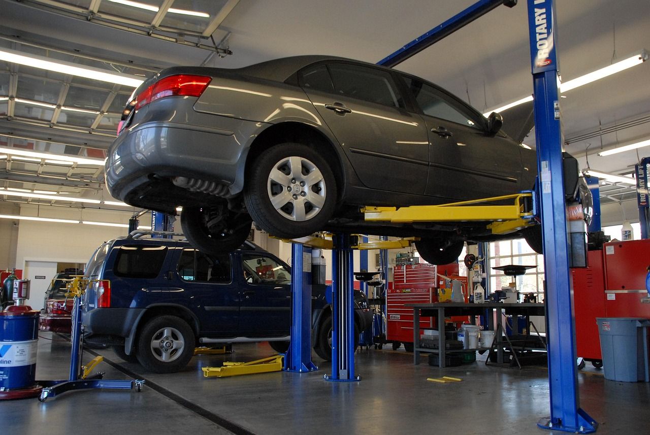 Carro no elevador da oficina Auto Center Pinhão, com outro carro e caixas de ferramentas ao fundo