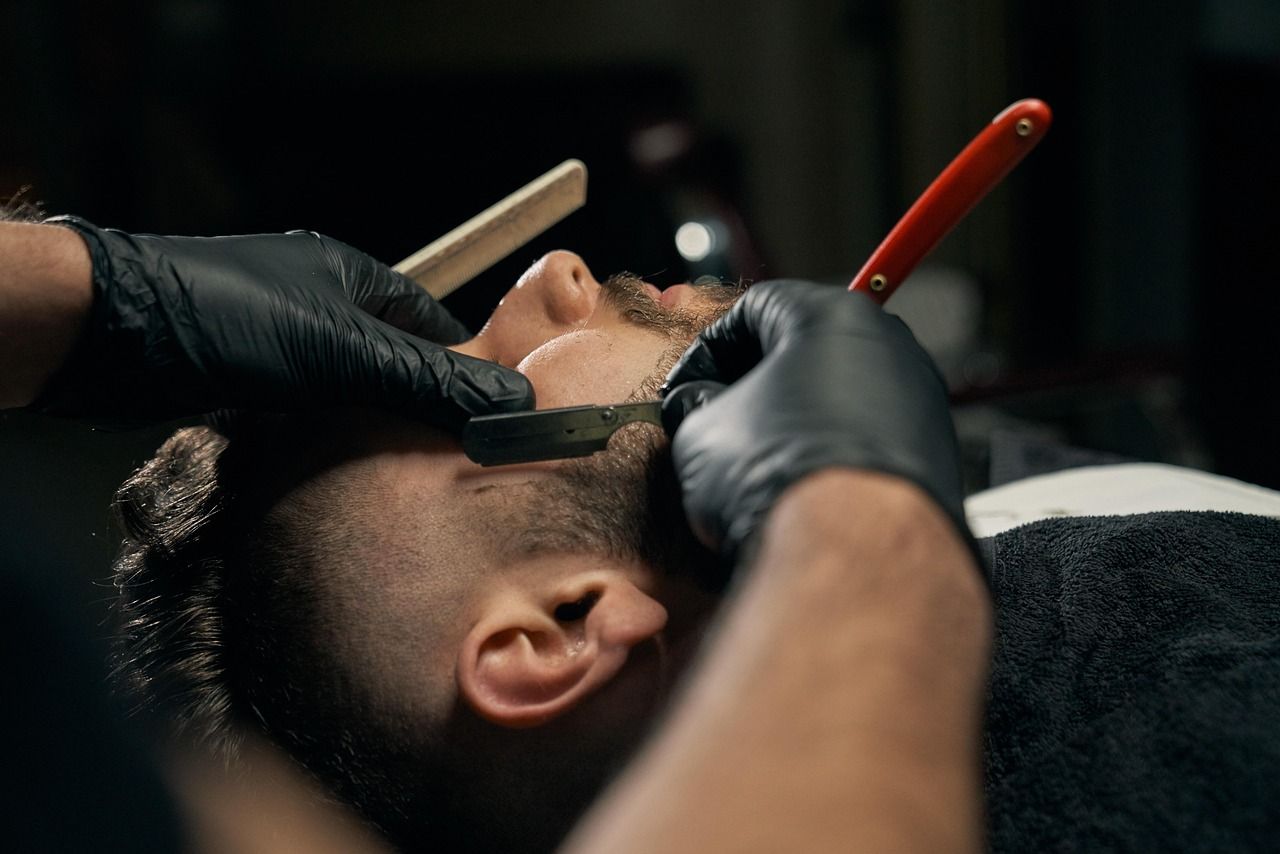 Barbeiro de luvas pretas fazendo a barba de um cliente com navalha