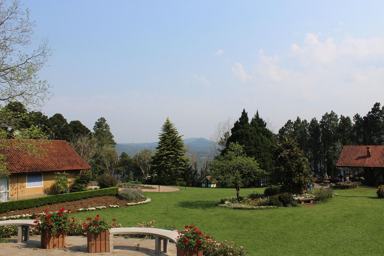 Gramado com canteiros de flores, casas de telhado de barro, pinheiros e a serra ao longe