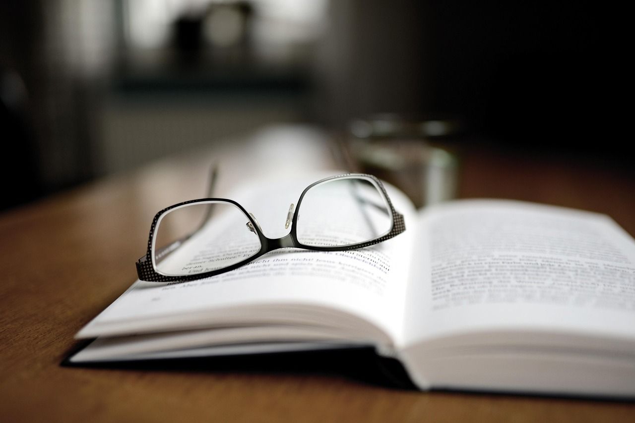 Livro aberto sobre a mesa de madeira, com um par de óculos em cima