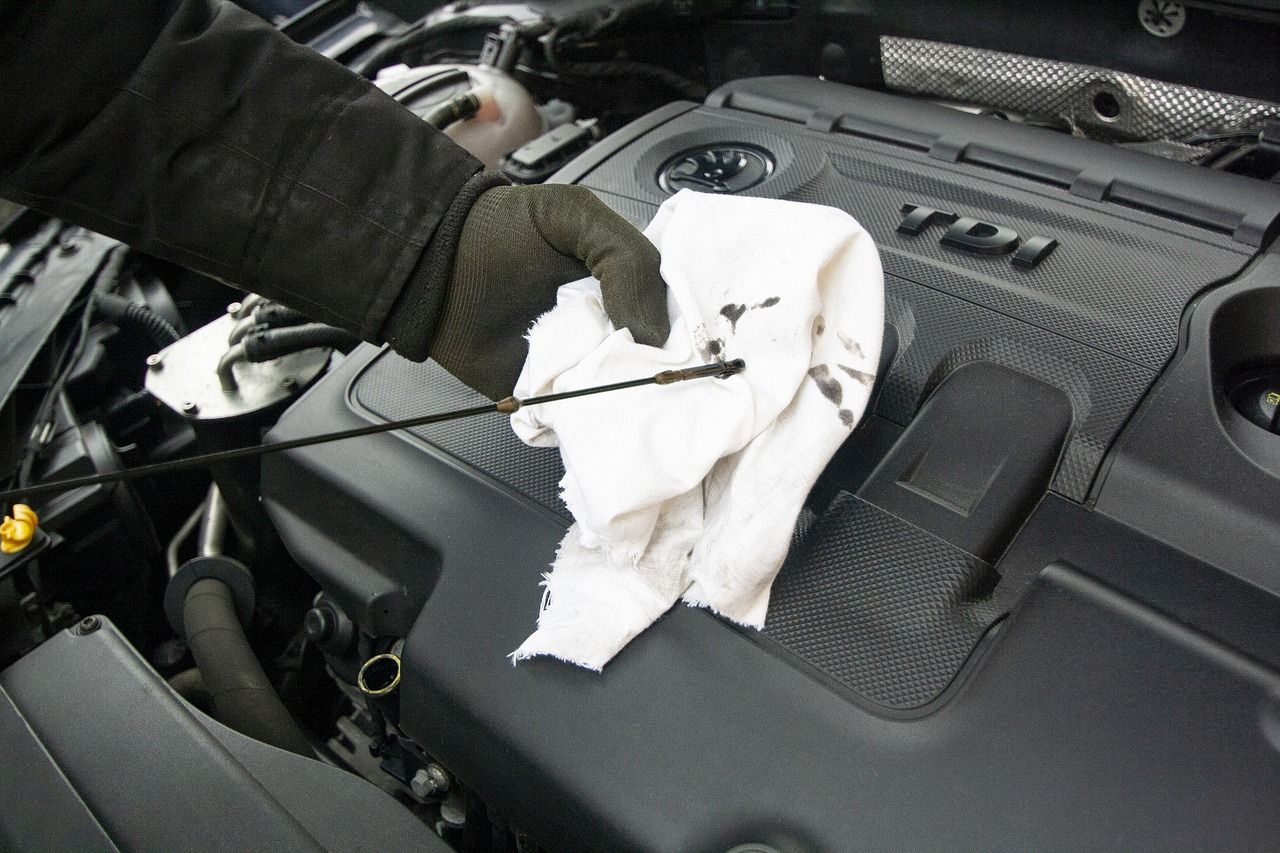 Mão com luva limpando a vareta de óleo com um pano, sobre o motor