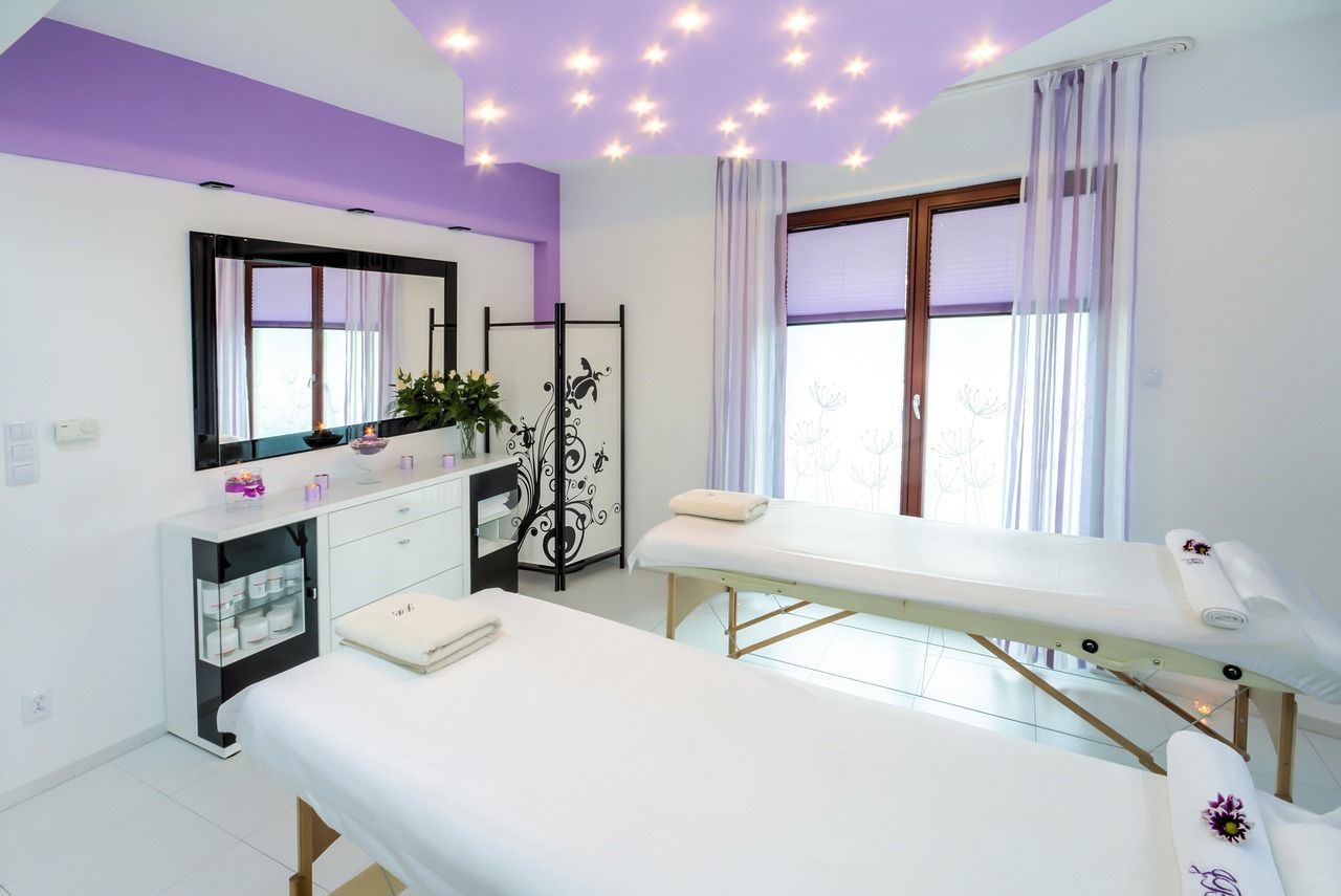 Sala clara com duas macas arrumadas, toalhas dobradas e porta de vidro