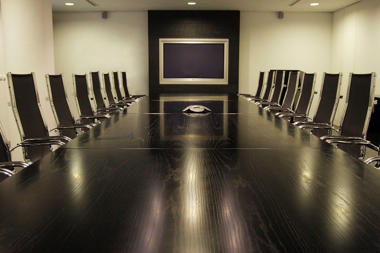 Sala de reuniões com mesa longa de madeira escura e cadeiras dos dois lados