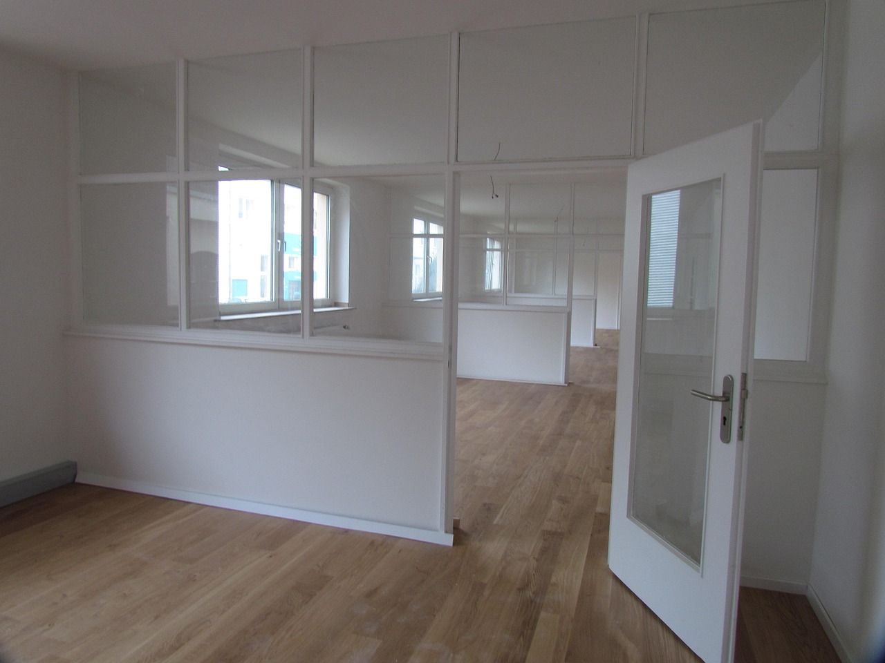 Sala vazia com piso de madeira, divisórias de vidro e janelas para a rua