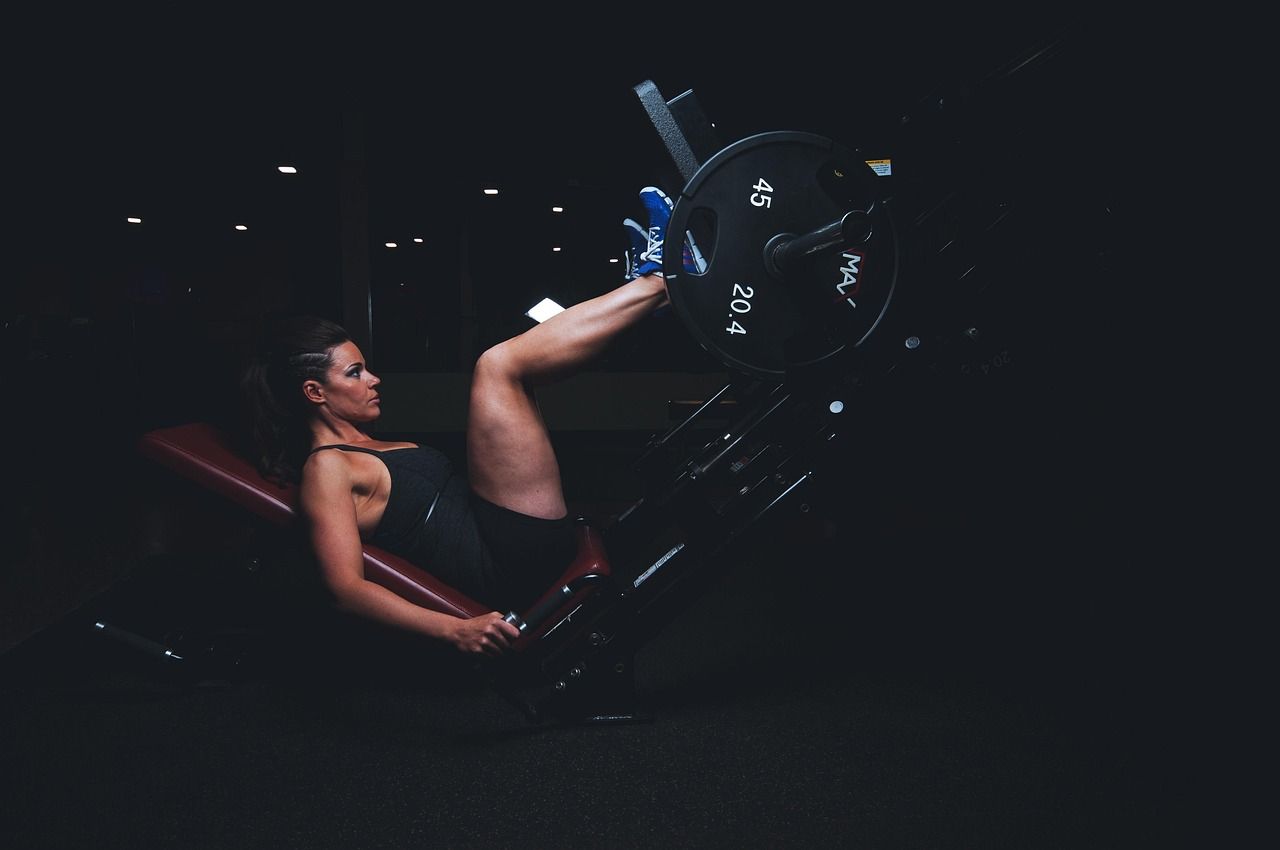 Aluna no leg press, no salão da academia à meia-luz